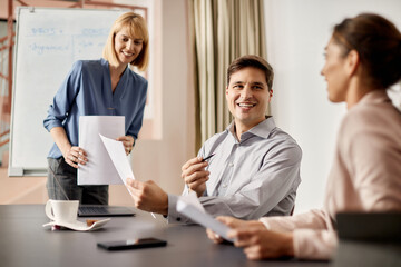 Happy businessman talks with female colleagues while analyzing reports on meeting in the office.