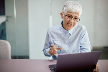 Mature businesswoman having glass of water while working on laptop in the office.