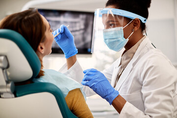 Black female dentist examines woman's teeth during appointment at dental clinic.