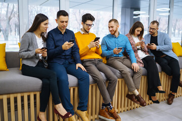 Group of young people using mobile phone. Business colegios sitting side by side in a modern office using digital devices. Study, business, technologies.