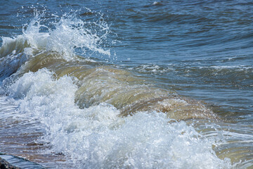 Sea waves crash against large rocks on the shore, forming large splashes