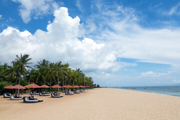 Empty beach with umbrellas and deck chairs. Palm trees. Beautiful summertime view seascape. Relax places island Bali island, Indonesia