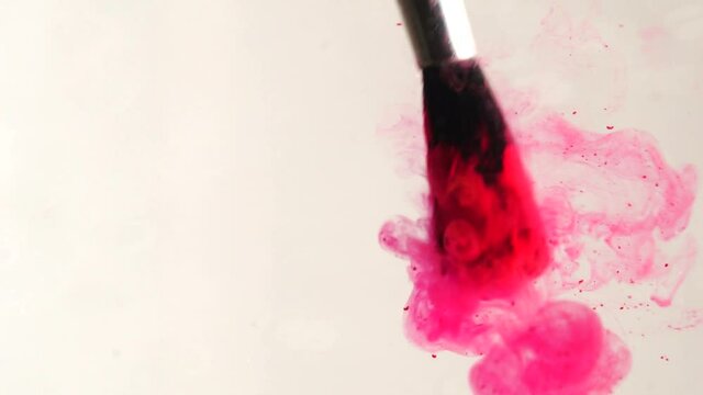 Cleaning a paint brush in water. Red paint dissolves in water, abstract gouache stains. Close up of a  paintbrush dipping into and rinsing in water. Paint in water.