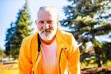 Naklejka na ściany i meble Senior man in orange sports wear doing stretching warming up outdoors sunny day in forest alone