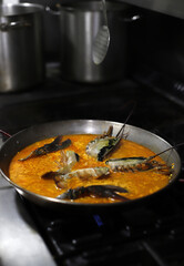 Paella de marisco con bogavante en paellera tradicional calentándose en fogón de cocina