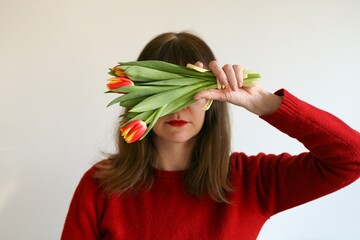 A woman holding flowers (tulips) in her hand and covering her eyes