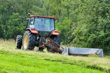 Tractor cutting grass in a field prior to drying and baling
