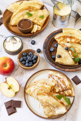 Celebrating Pancake day, healthy breakfast. Homemade sweet crepes with blueberries, ricotta, apples, bananas and chocolate on a marble tabletop.