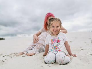 young attractive mother with pink hair and a happy child in the background of a sandy beach. hot sunny day, white sand, summer vacation, day off. Family holiday