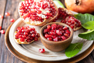 Ripe juicy pomegranate fruits in a wooden bowl on a rustic table closeup. Diet and healthy food.