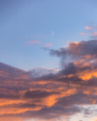 Sliver of a crescent moon rising above colorful sunset clouds