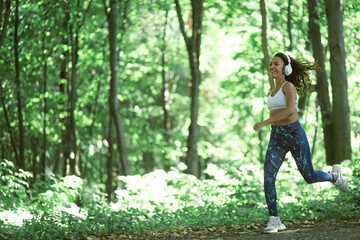 Beautiful young afro girl running in the park in summer listening to music with headphones