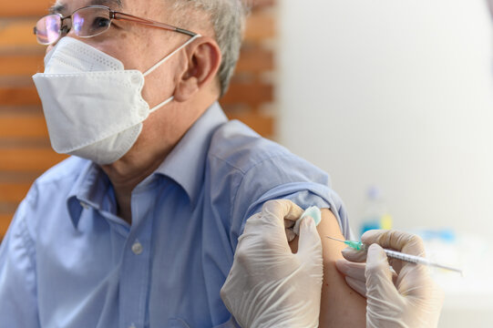 Close up hand of Asian woman nurse injecting covid-19 vaccine to senior Thai man patient wearing mask in clinic or health care center. Coronavirus pandemic protection or health care medical concept.