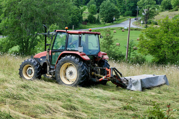 Tractor cutting grass in a field prior to drying and baling
