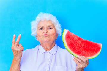 mature woman with snow white grey white hair in blue shirt holding watermelon in studio background
