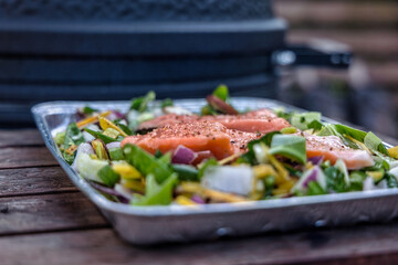 Aluminum griddle plate on wooden side tray of barbecue with salmon and vegetables