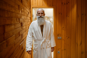 Smiling bearded man in bathrobe in sauna - obrazy, fototapety, plakaty
