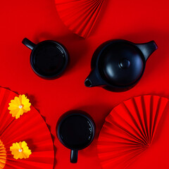 Chinese New year Classy red square composition with teapot, teacups and paper fans with yellow flowers.