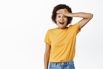 Portrait of excited, surprised black girl remember smth, hold hand on forehead and looking amazed, receive great news, look with happy disbelief, white background