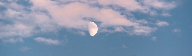 The moon in the blue sky behind the clouds. Day moon.