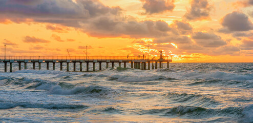 Pier on the sea, orange sunset on the background