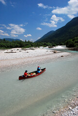 Red canoe with two people paddling down the clear river Isar with its white pebble riverbed in the...