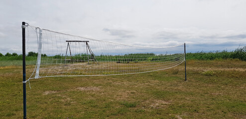 volleyball net in the field in summer against the background of grass, blue sky and swings