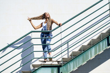 Black girl on an urban staircase, holding her coloured braids. Typical African hairstyle.