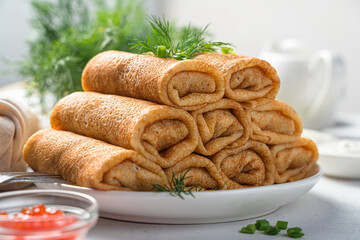 A stack of rolls of pancakes with meat on a white plate decorated with fresh dill.