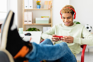 Addicted young teenage man playing video games on mobile phone app - Relaxed 20s hispanic young guy...