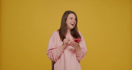 Happy young girl holding phone communicating in social media laughing having fun on yellow background. Dating app ad