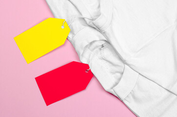 Two white T-shirts on a pink background with blank price tags. Blank label on clothes