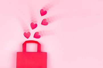 Online shopping concept. Top view of gift bag and pink paper hearts on pink background with ripple effect, copy space, flat lay. Background for Valentine's Day, Birthday, Mother's Day