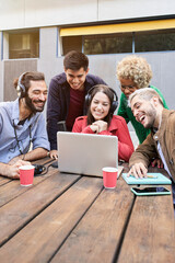 Vertical photo. Video call of a Group of young smiling people outdoors watching a video on the laptop. Colleagues broadcasting togethers