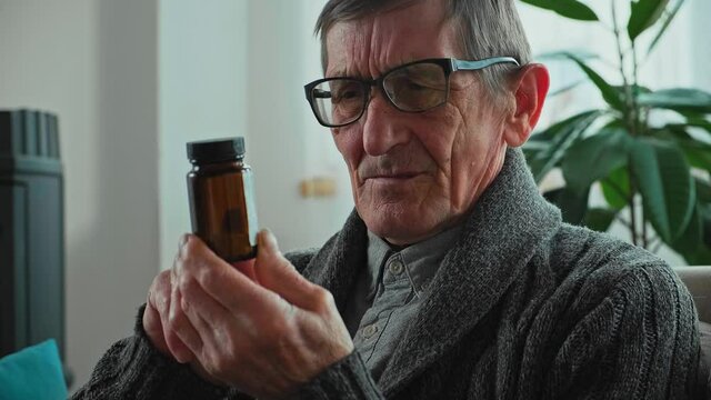 Elderly senior in eyeglasses holding a bottle of pills in hands for the treatment of visual impairment, tensely reads the instructions on bottle