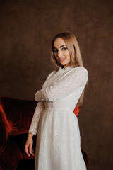 Portrait of a girl in a white beautiful dress on a brown background and a red velvet chair