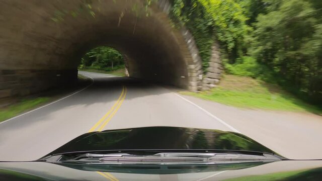 Passenger vehicle driving under a stone bridge on asphalt road in the middle of forest, Great Smoky Mountains, Tennessee. Road trip concept