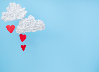Fototapeta na wymiar White clouds and red paper hearts in the form of rain on a blue background. Abstract background with paper-cut shapes. Sainte Valentine, mother's day, birthday greeting cards, invitation
