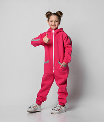 stylish girl in a sports pink suit with reflective stripes, shows a thumbs up. stylish cotton tracksuit, pajamas with a hood, a fashion model for children.