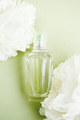 Fototapeta na wymiar Transparent mockup glass bottle with perfume among fresh white peony flowers on light green pastel color