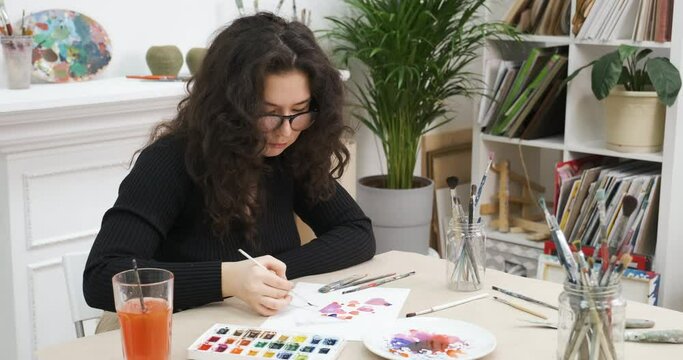 Crafting handmade picture with hearts for St. Valentine's Day. Girl drawing a postcard for Valentines Day in art workshop with brush and watercolor. Preparing card for beloved.