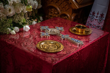 Cross and other accessories on the table with red cloth in the orthodox church, religion, faith and wedding traditions