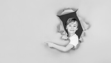 Kid looks through hole. Blonde boy looks through ripped paper. Boy in red paper hole pointing with...