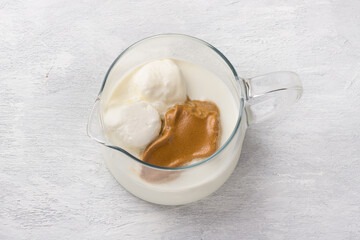 Glass jug with milk, vanilla ice cream and whipped coffee foam on light gray background. Preparing trendy dalgona coffee drink