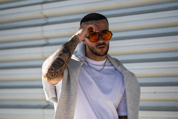 chico con tatuajes y gafas de sol naranjas mirando al horizonte