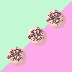 Three pink donuts with chocolate sprinkles, on a green and purple background