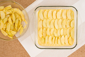 Apple cake with biscuit base recipe. Peeled apple slices on a top of batter close up in a glass baking dish, directly from above