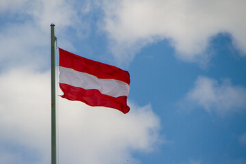 Vienna, Austria, July 21, 2021. Austrian flag on blue sky background. The Austrian flag consists of a white band surrounded by two red bands.