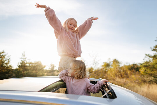 Sisters standing in sunroof of car
