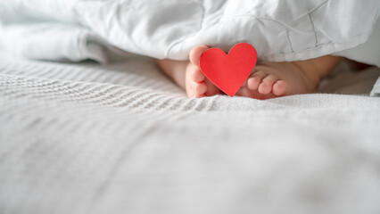 Children's heels, baby, lie on the bed under the blanket with a tag on the finger, with a heart. Valentine's Day.